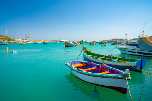 Barcos tradicionais malteses coloridos ancorados em água turquesa.