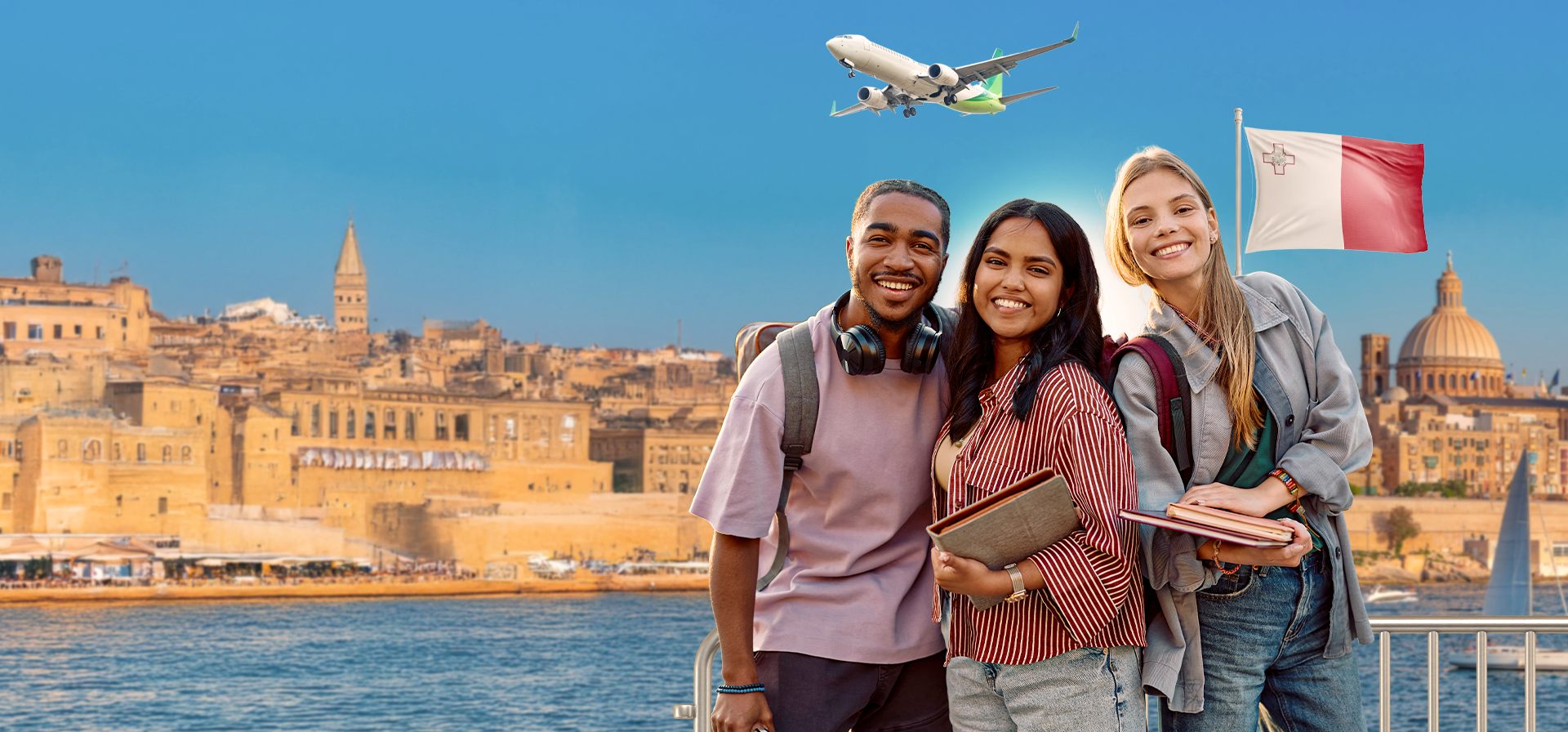 Três estudantes sorrindo em frente à orla de Valletta, em Malta, com a bandeira maltesa e um avião ao fundo.